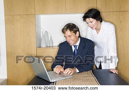 Businessman using a laptop with a businesswoman standing beside him View Large Photo Image Stock Image - Businessman using a laptop with a businesswoman standing beside him. Fotosearch