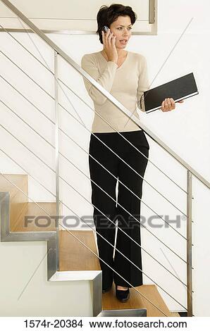 Businesswoman standing on a staircase and talking on a mobile phone View Large Photo Image Picture - Businesswoman standing on a staircase and talking on a mobile phone. Fotosearch