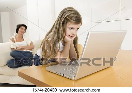 Close-up of a girl looking at a laptop with her mother sitting in the background View Large Photo Image Stock Image - Close-up of a girl looking at a laptop with her mother sitting in the background. Fotosearch
