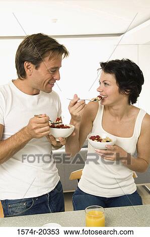 Stock Image - Close-up of a young couple holding bowls of fruit salad and smiling. Fotosearch
