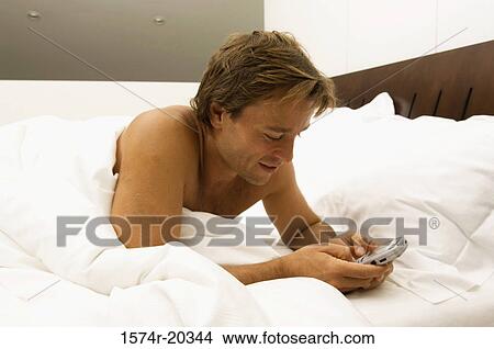 Close-up of a young man operating a mobile phone in the bed View Large Photo Image Picture - Close-up of a young man operating a mobile phone in the bed. Fotosearch