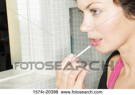 Close-up of a young woman applying lipstick to her lips View Large Photo Image Stock Photo - Close-up of a young woman applying lipstick to her lips. Fotosearch