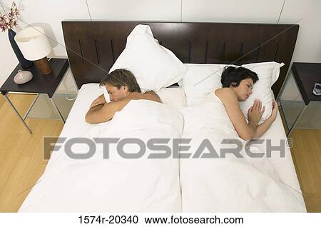 Stock Image - High angle view of a young couple lying in the bed and looking sad. Fotosearch