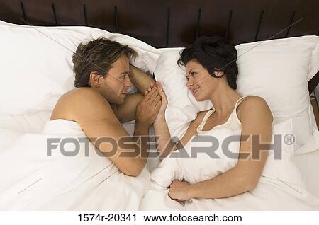 Stock Image - High angle view of a young couple lying in the bed and smiling. Fotosearch