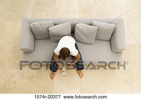 High angle view of a young man sitting on a couch with a remote control View Large Photo Image Stock Photo - High angle view of a young man sitting on a couch with a remote control. Fotosearch