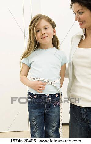 Stock Photography - Portrait of a girl measuring her waist with her mother standing beside her. Fotosearch