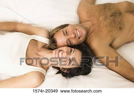 Stock Photo - Portrait of a young couple lying in the bed and smiling. Fotosearch