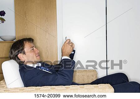 Side profile of a businessman sitting in an armchair and holding a mobile phone View Large Photo Image Stock Photo - Side profile of a businessman sitting in an armchair and holding a mobile phone. Fotosearch