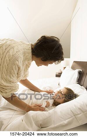 Side profile of a young woman bending over her daughter lying on the bed View Large Photo Image Picture - Side profile of a young woman bending over her daughter lying on the bed. Fotosearch