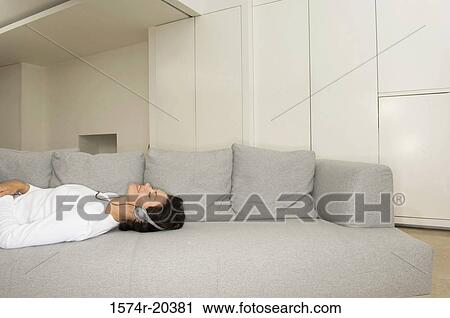 Side profile of a young woman listening to music on a couch View Large Photo Image Stock Image - Side profile of a young woman listening to music on a couch. Fotosearch