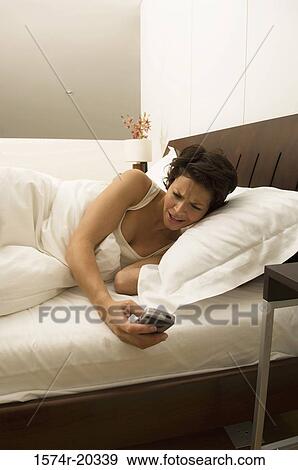 Stock Photo - Young woman holding a mobile phone in the bed. Fotosearch