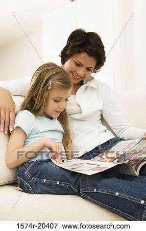 Stock Photo - Young woman reading a magazine with her daughter on a couch. Fotosearch