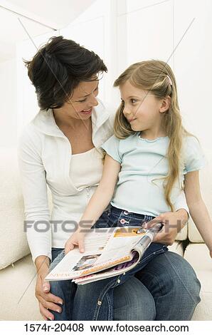 Stock Photo - Young woman reading a magazine with her daughter on a couch. Fotosearch