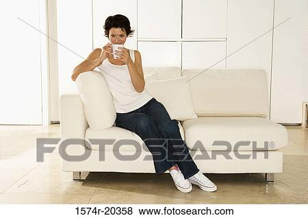 Stock Photo - Young woman sitting on a couch with a cup. Fotosearch