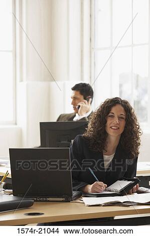 Portrait of a businesswoman holding a pen with a businessman talking on a mobile phone in the background View Large Photo Image Picture - Portrait of a businesswoman holding a pen with a businessman talking on a mobile phone in the background. Fotosearch