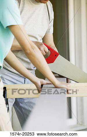 Close-up of a woman standing with a man cutting a plank with a saw View Large Photo Image Stock Image - Close-up of a woman standing with a man cutting a plank with a saw. Fotosearch