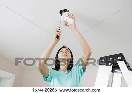 Stock Photography - Low angle view of a young woman fixing a light fixture. Fotosearch