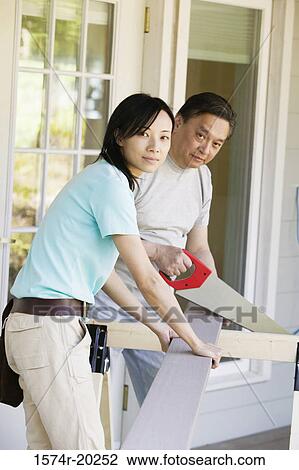 Stock Image - Mid adult man cutting a plank with a saw. Fotosearch