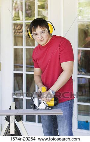 Portrait of a young man cutting a plank with an electric saw View Large Photo Image Picture - Portrait of a young man cutting a plank with an electric saw. Fotosearch