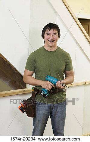 Picture - Portrait of a young man holding a drill smiling. Fotosearch