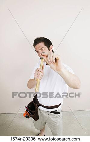 Stock Photograph - Portrait of a young man holding a nail and a hammer. Fotosearch