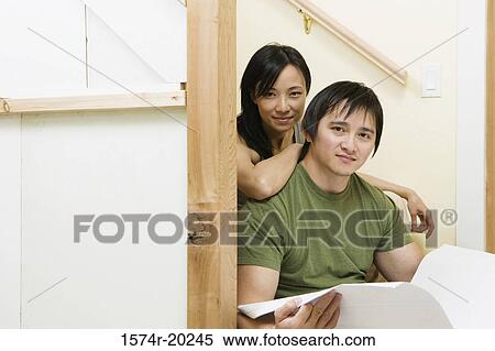 Stock Photography - Portrait of a young man holding a blueprint with a young woman leaning on him. Fotosearch