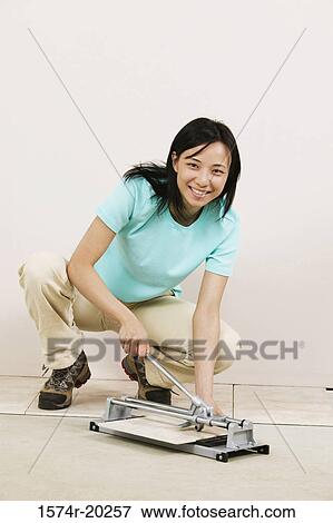 Stock Photo - Portrait of a young woman cutting tile with a tile cutter. Fotosearch