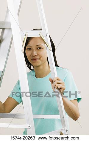 Stock Image - Portrait of a young woman holding a ladder. Fotosearch