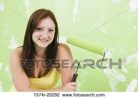 Stock Image - Portrait of a young woman holding a paint roller. Fotosearch