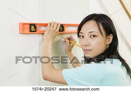 Portrait of a young woman using spirit level to mark on a wall View Large Photo Image Stock Photo - Portrait of a young woman using spirit level to mark on a wall. Fotosearch