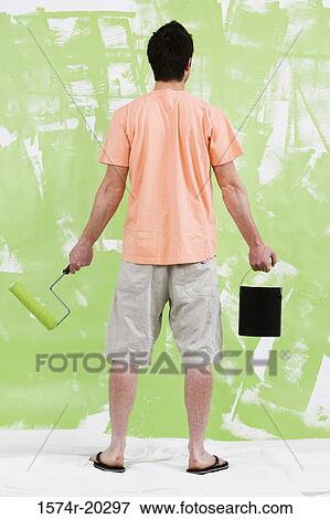 Stock Photo - Rear view of a young man holding a paint can and a paint roller. Fotosearch
