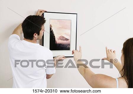 Rear view of a young man putting up a painting on a wall with a young woman's guidance View Large Photo Image Stock Image - Rear view of a young man putting up a painting on a wall with a young woman's guidance. Fotosearch