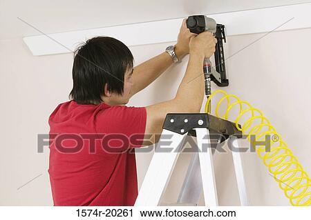 Stock Image - Rear view of a young man using a drill on a wall. Fotosearch