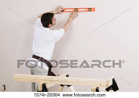 Rear view of a young man using a spirit level to mark on a wall View Large Photo Image Picture - Rear view of a young man using a spirit level to mark on a wall. Fotosearch