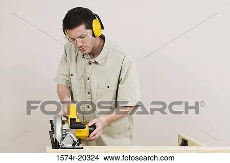 Young man sawing a plank with an electric saw View Large Photo Image Picture - Young man sawing a plank with an electric saw. Fotosearch