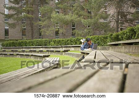 Stock Photo - College student lying on a bench and using a laptop. Fotosearch