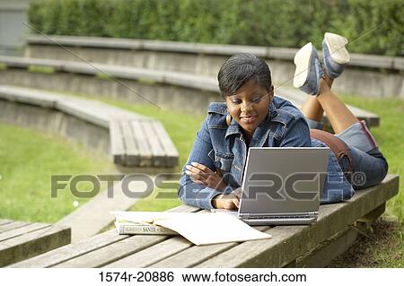 Stock Photograph - College student lying on a bench and using a laptop. Fotosearch