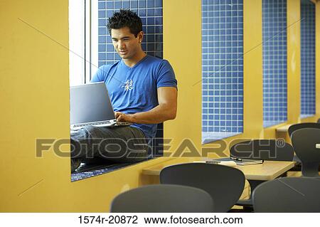 Stock Image - College student sitting on a window ledge and using a laptop. Fotosearch