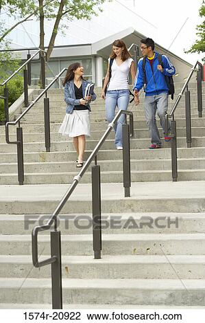 Stock Image - Low angle view of three college students moving down a staircase and smiling. Fotosearch