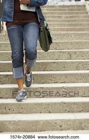 Picture - Low section view of a college student moving down a staircase and carrying books. Fotosearch
