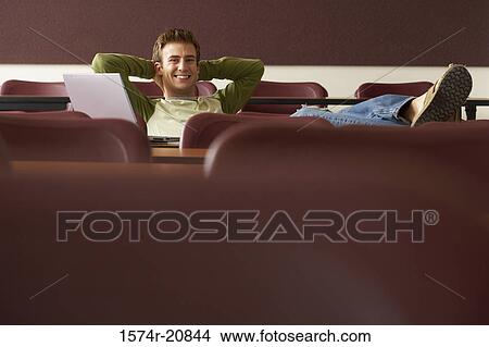 Portrait of a college student sitting in a lecture hall with his hands behind his head View Large Photo Image Picture - Portrait of a college student sitting in a lecture hall with his hands behind his head. Fotosearch