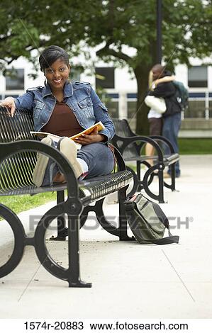 Stock Image - Portrait of a college student sitting on a bench and smiling. Fotosearch