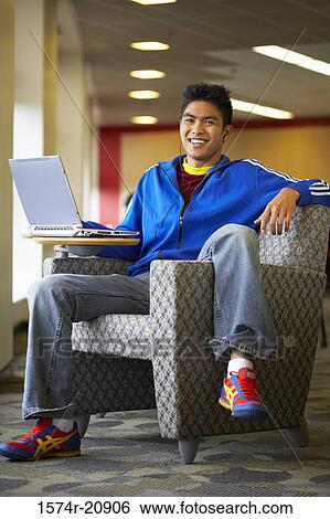 Stock Photograph - Portrait of a college student sitting in an armchair with a laptop. Fotosearch