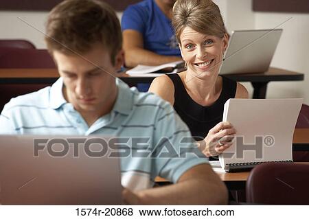 Portrait of a college student smiling with another student sitting in front of her and using a laptop View Large Photo Image Stock Photo - Portrait of a college student smiling with another student sitting in front of her and using a laptop. Fotosearch