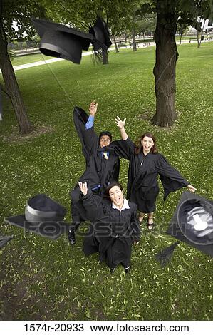 Stock Image - Portrait of two female graduates and a male graduate throwing their mortarboards in the air. Fotosearch