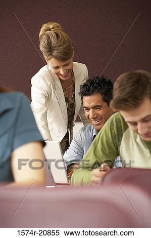 Professor looking at a laptop of a college student in a lecture hall and smiling View Large Photo Image Stock Photography - Professor looking at a laptop of a college student in a lecture hall and smiling. Fotosearch