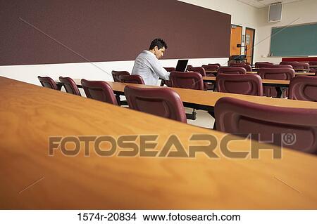 Picture - Side profile of a college student sitting in a lecture hall and using a laptop. Fotosearch