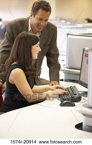 Picture - Side profile of a college student working on a computer with her professor standing beside her. Fotosearch