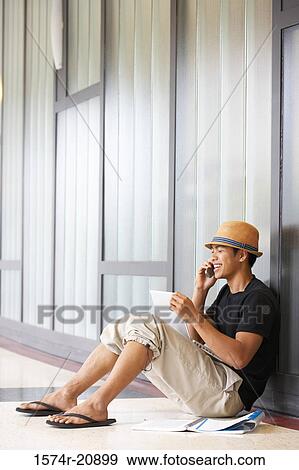 Stock Photo - Side profile of a college student sitting in a corridor and talking on a mobile phone. Fotosearch