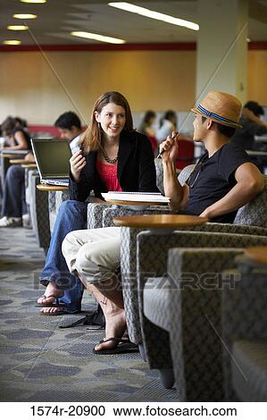 Stock Image - Side profile of two college students sitting in a lecture hall and talking to each other. Fotosearch